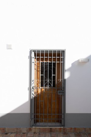 Foto de Puerta de madera a la antigua con una parrilla de seguridad de metal mitad a la luz del sol brillante mitad a la sombra - Imagen libre de derechos
