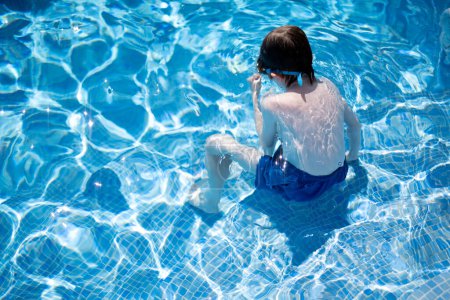Boy sitting on the steps of a swimming pool with his whole body under water