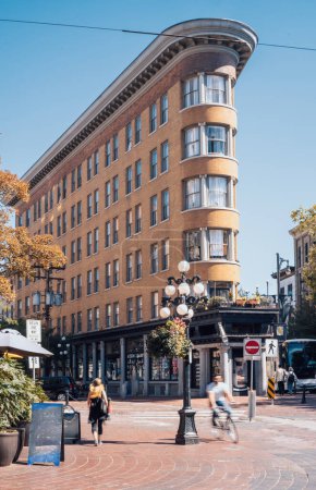 Los peatones se mueven frente a un edificio histórico distintivo y curvo en un día soleado en Vancouver