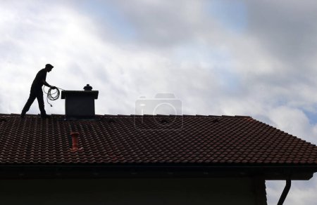 Téléchargez les photos : A chimney sweep cleans the chimney on a house roof - en image libre de droit