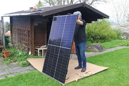 Téléchargez les photos : Un homme veut monter un petit système solaire sur un abri de jardin - en image libre de droit