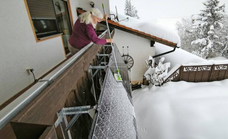 Eine Frau beseitigt im Winter Schnee von einem Balkon