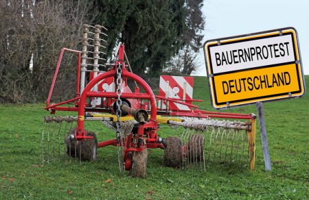 Schild mit Bauernprotest Deutschland und einer geparkten Landmaschine auf einem Feld