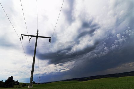 Cielo oscuro sobre un pilón de electricidad en un campo. Tiempos oscuros para la fuente de alimentación en Alemania