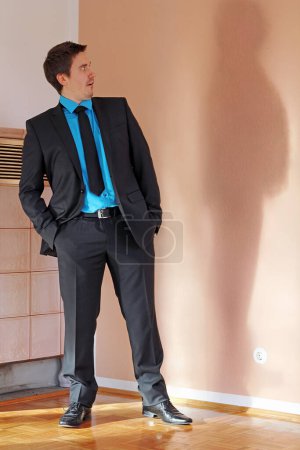 A man in a suit is frightened by his thicker shadow