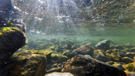 Unterwasseraufnahme vom Grund eines Flusses, wo die Sonnenstrahlen ins Wasser fallen