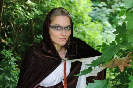 Eine Frau als mittelalterliche Jägerin in einem Kleid mit Kapuze versteckt sich im Wald