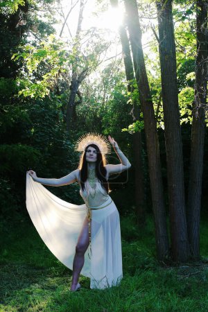Eine Frau als Göttin steht im Wald, im Gegenlicht der Sonne