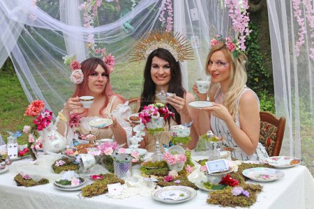 Tres mujeres vestidas de elfos o hadas se sientan felices en una mesa de té