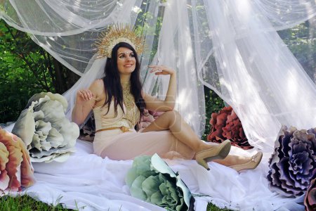 A woman dressed as a goddess lies smiling on a bed with flowers