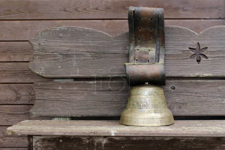 A large old brass cowbell on a wooden bench
