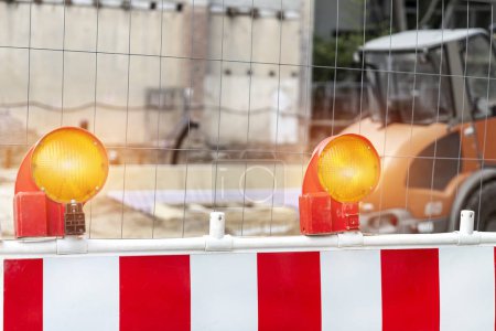 Photo for Close-up detail view orange flasher safety blinker light barrier against fence construction site work area. Security equipmnent barricade fuse lamp city street building construction machinery traffic. - Royalty Free Image