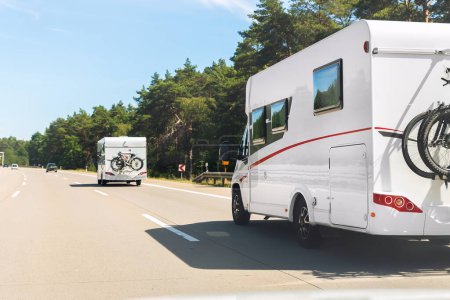 Scenic view big modern white family rv camper van vehicle driving on european highway road against blue sky in summer day. Rving motorhome lifestyle travel and adventure tourism trip journey concept.