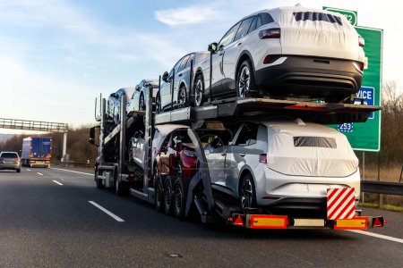 Photo for Tow truck car carrier semi trailer on highway carrying batch of new wrapped electric SUVs on motorway road at sunset evening time. Business distribution logistics service. Lorry driving highway. - Royalty Free Image