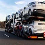 Tow truck car carrier semi trailer on highway carrying batch of new wrapped electric SUVs on motorway road at sunset evening time. Business distribution logistics service. Lorry driving highway.