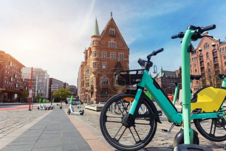 Photo for Scenic view electric rental bicycle bikes parked St. Annenplatz in old Hafencity Speicherstadt quartier haven Hanburg city street warm sunset sunlight. Healthy ecology urban transport infrastructure. - Royalty Free Image