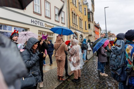 Téléchargez les photos : Erfurt, Allemagne - 11 février 2024 : Carnaval traditionnel allemand Fasching 2024 en Thuringe. Les gens ville rue célébrer festival danse avoir plaisir centre-ville flottant par temps de pluie forte. - en image libre de droit