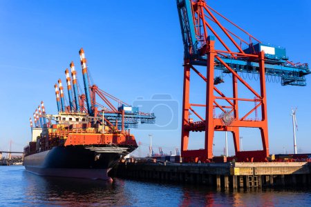Vista panorámica barco contenedor de carga gigante cargando puerto de la ciudad de Hamburgo puerto contra grúas portuarias luces cálidas puesta del sol por la noche. Comercio global flete flete mercantil envío y logística antecedentes.