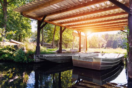 Old metal boat moored under shed shelter wooden canopy rustic boathouse at countryside in Spreewald canal national biosphere reserve house. Scenic Vintage water transport warm morning sunrise.