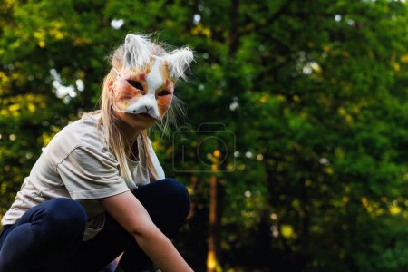 Cute young little kid girl wear cat furry mask enjoy have fun playing outdoors in forest street park. Children therian wild animal character trendy fan culture. Teenager social expression hobby.