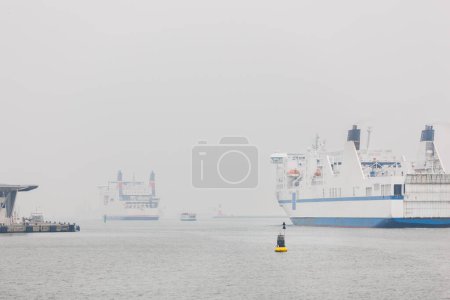 Big modern ferry ship navigate from Rostock harbor Warnemunde bay foggy spring autumn morning misty weather scenic view background. Maritime traffic liner passenger cargo vessel at Baltic sea Germany.