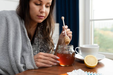 Kranke Frau steckt etwas Honig in ihren Tee
