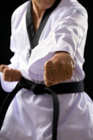 Foto de Cinturón rojo negro TaeKwonDo Karate atleta masculino hombre espectáculo tradicional lucha plantea ponche sobre fondo negro de cerca en ponche - Imagen libre de derechos