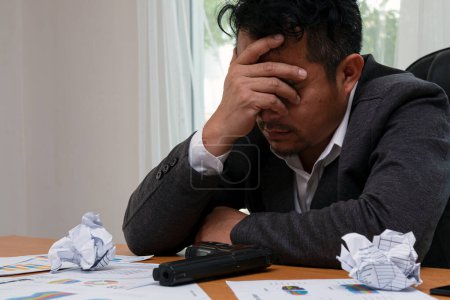 Photo for Criminal Tension in Business World: Stressed Asian Businessman sleep with holding Gun and many information graph sheet on desk in office - Royalty Free Image