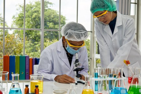 Two scientists are deeply engrossed in conducting chemical experiments, surrounded by colorful reagents in a bright laboratory with a greenery backdrop
