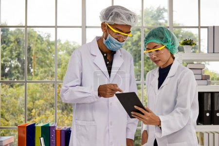 Two lab researchers are collaborating, with one pointing at a digital tablet, in a modern laboratory setting filled with natural light