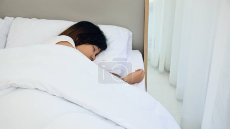 Asiatique jeune femme jouit d'un sommeil reposant, enveloppé dans une literie blanche douce, dans un cadre lumineux et aéré chambre