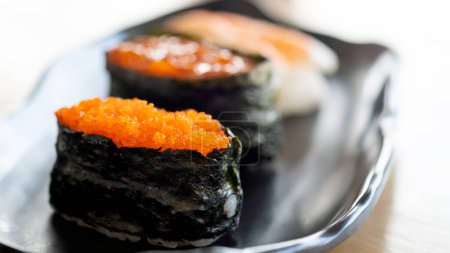 Skupione zbliżenie tobiko gunkan sushi, japoński przysmak, na eleganckiej płycie ceramicznej z miękkim oświetleniem podkreślając jego teksturę i kolor