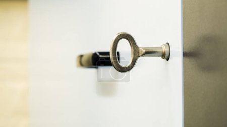 A modern silver key inserted into a door lock with a blurred black handle in the background, symbolizing access and security