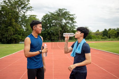 Two young Asian teenage athletes drinking water and resting during a break in track and field training, highlighting the importance of hydration