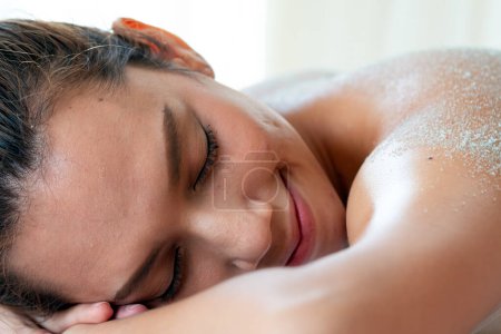Asiatische ruhige Frau mit friedlichem Gesichtsausdruck legt sich hin und genießt eine Salzpeeling-Wellness-Behandlung zur Entspannung und Hautpflege