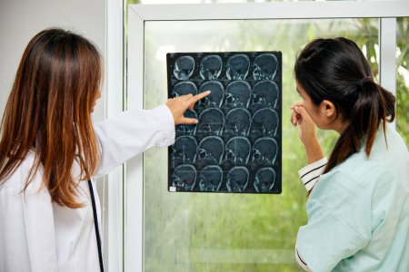 Dos doctora en bata blanca explicando resonancias magnéticas cerebrales y discutiendo en consultorio médico, destacando consulta diagnóstica y salud neurológica