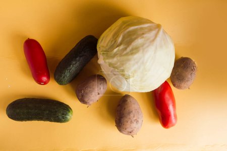 Kohl, Kartoffeln, Gurken und Tomaten auf gelbem Hintergrund, erhöhter Blick