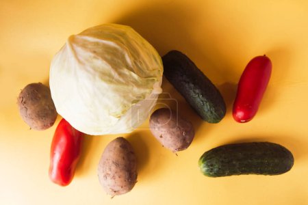 Cabbage, potatoes, cucumbers and tomatoes on yellow background, elevanted view