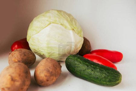 Pepinos, patatas, tomates y col crudos sobre fondo blanco