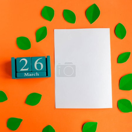 26. März blauer Würfel-Kalender und weiße Mockup-Rohlinge auf leuchtend orangefarbenem Hintergrund