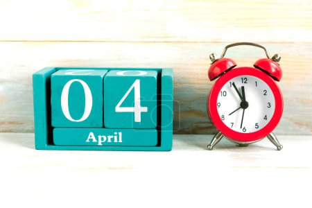 April 4. Blue cube calendar with month and date and red alarm clock on wooden background