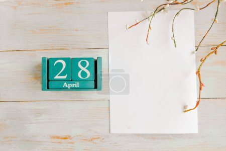 28. April. Blauer Würfel-Kalender mit Monat und Datum und weißem Mockup-Rohling auf Holzgrund