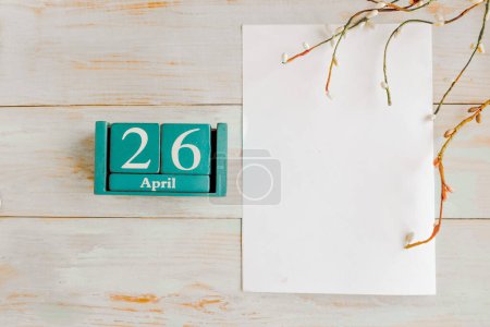 26. April. Blauer Würfel-Kalender mit Monat und Datum und weißem Mockup-Rohling auf Holzgrund