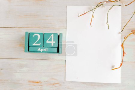 24 de abril. Calendario cubo azul con mes y fecha y maqueta blanca en blanco sobre fondo de madera