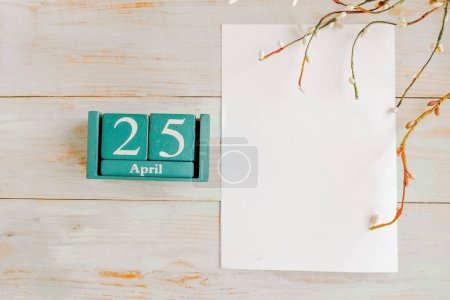 25 de abril. Calendario cubo azul con mes y fecha y maqueta blanca en blanco sobre fondo de madera