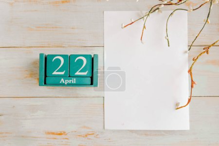 April 22. Blue cube calendar with month and date and white mockup blank on wooden background