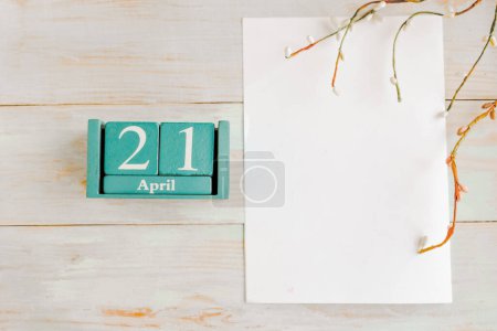 April 21. Blue cube calendar with month and date and white mockup blank on wooden background