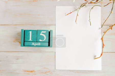 15 de abril. Calendario cubo azul con mes y fecha y maqueta blanca en blanco sobre fondo de madera