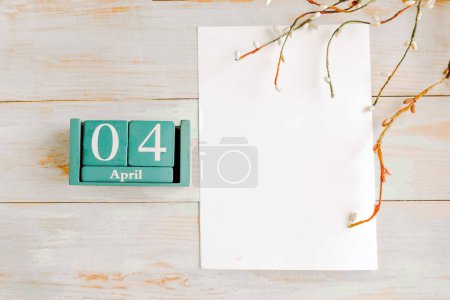 April 4. Blue cube calendar with month and date and white mockup blank on wooden background