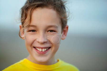Foto de Close-up portrait of a cheerful boy with curly fair hair. Child with a big smile looking to the camera, blurry background - Imagen libre de derechos